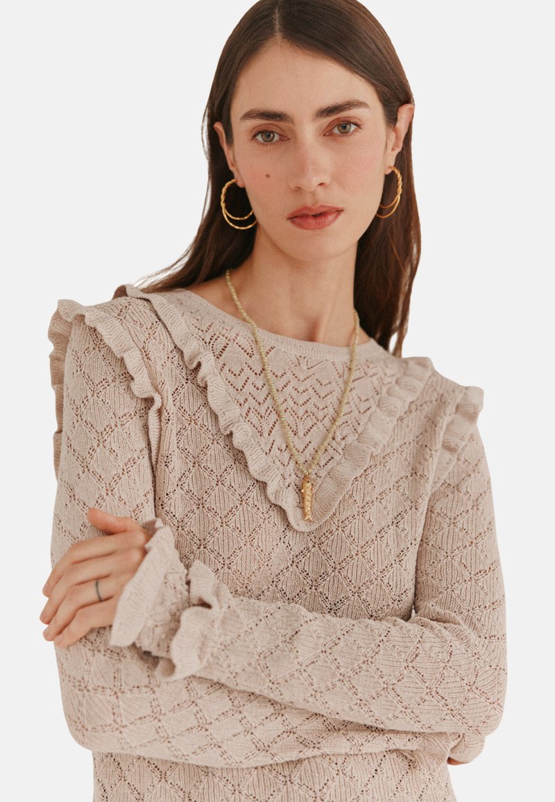 Maglione lavorato a maglia beige chiaro con un motivo a diamante testurizzato, scollatura e polsini arricciati, maniche lunghe e vestibilità comoda.