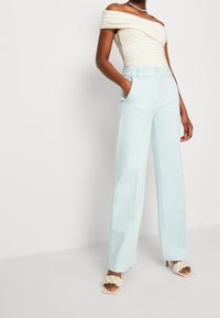 Off-shoulder crèmekleurig topje gecombineerd met lichtblauwe wijde broek met zijzakken, een zachte stof en een getailleerde pasvorm.