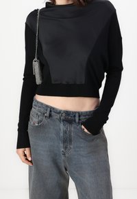Czarny krótki sweter z satynową wstawką z przodu, zestawiony z szarymi jeansami. Sweter ma długie rękawy i ściągacze przy mankietach.