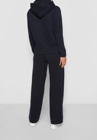 Sudadera azul marino con bolsillo canguro y capucha ajustable con cordón, complementada con pantalones de chándal de pierna ancha a juego. Tela de mezcla de algodón suave.