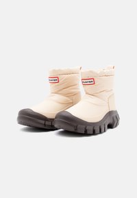 Beige szigetelt bokacsizmák párnázott felső résszel, barna gumitalppal és texturált oldalakkal. A "HUNTER" márkaneve látható a felső részen.