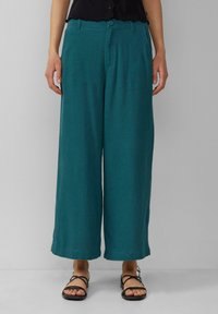Teal, wide-leg pants made of lightweight fabric, featuring a button closure and visible seams. Worn with black strappy sandals.