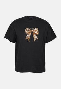 Camiseta negra de manga corta con un gráfico de un lazo de print de leopardo en tonos de marrón y dorado, con el texto "No seas tímido" encima del lazo.