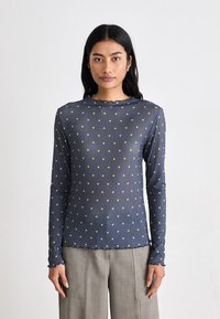 Maglietta a maniche lunghe blu navy con pois verdi, texture a coste e scollatura a onda; silhouette aderente e tessuto elasticizzato.
