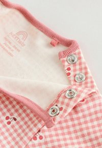 Rózsaszín és fehér kockás baba ruhadarab cseresznyemintákkal, rózsaszín szegéllyel és három fém patentgombbal a nyakkivágás szélén.
