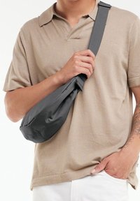 Sac bandoulière gris et profilé en tissu doux, doté d'une sangle réglable et d'une forme arrondie pour une meilleure facilité de port.