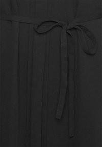 Tecido preto com pregas verticais, apresentando um cinto laço na cintura. Textura suave e cor consistente por toda a peça.