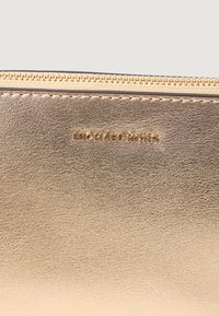 Portofel din piele metalizată aurie, cu o textură netedă, având logo-ul "MICHAEL KORS" embosat în același ton de aur. Închidere cu fermoar pe partea de sus.