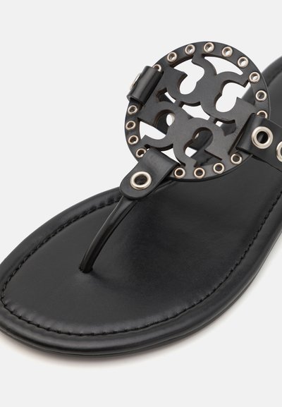 Sandale en cuir noir avec un design découpé circulaire, accents métalliques et une lanière entre les orteils. Texture lisse, semelle intérieure rembourrée et bords cousus.