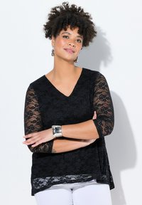 Top in pizzo nero con maniche a tre quarti, design a V, orlo stratificato, caratterizzato da un motivo in pizzo testurizzato. Abbinato a pantaloni bianchi.
