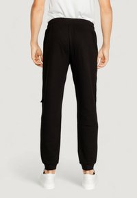 Black jogger pants in soft fabric, tapered fit, featuring elastic waistband and cuffs, paired with white sneakers on a neutral background.