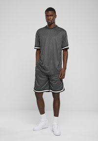 Ensemble de sport noir et blanc à rayures comprenant un haut à manches courtes et un short, avec des accents de bord contrastants. Porté avec des baskets blanches.