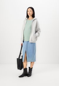 Grå sweatshirt med huva, ljusgrön ribbad topp, denimkjol med slits fram, svarta ankelboots och en svart tote-väska.