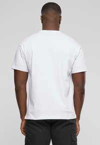 White cotton t-shirt with short sleeves, featuring a crew neckline and a straight hem, worn by a person, viewed from the back.