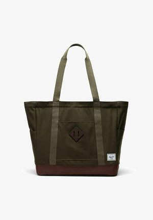 Sac fourre-tout en toile vert olive avec base marron, deux longues anses, poche avant, et petite étiquette de marque blanche rectangulaire en bas à droite.