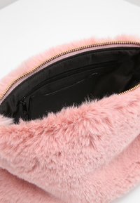 Růžová kabelka z umělého kožešiny s černým interiérem, která má zlatý zip a měkkou texturu. V interiéru je zipová kapsa na úložný prostor.