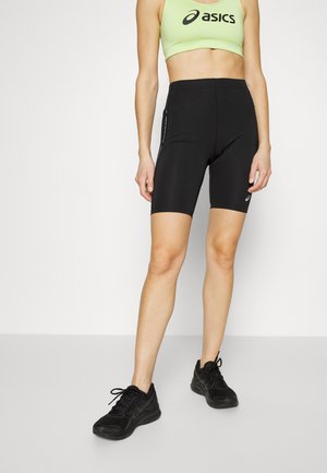 Shorts de cyclisme noirs en tissu extensible, avec une taille haute et des poches zippées sur le côté. Assortis à un soutien-gorge de sport vert clair.