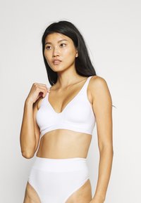 Soutien-gorge blanc sans couture avec des bretelles larges et un design en V, associé à des culottes blanches taille haute. Texture lisse et style minimaliste.