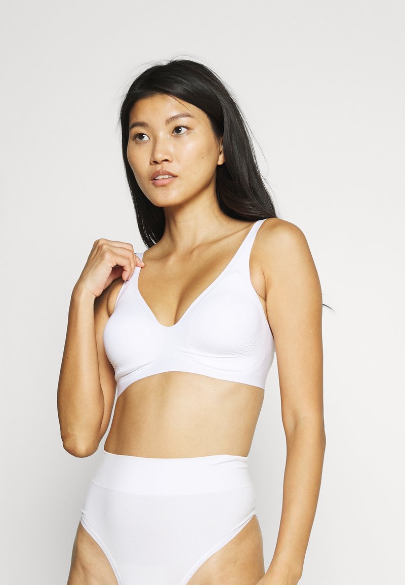 Soutien-gorge blanc sans couture avec des bretelles larges et un design en V, associé à des culottes blanches taille haute. Texture lisse et style minimaliste.