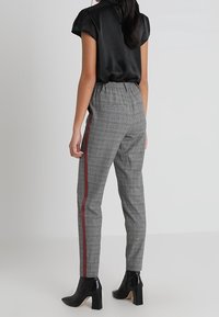 Grå rutiga byxor med rak passform, med en röd sidremsa. Matchas med en svart satinblus och svarta ankelstövlar.