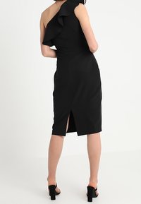 Schwarzes Kleid mit einem Schulterträger und einem rüschenden Akzent. Enganliegende Silhouette mit einem Schlitz hinten für Bewegungsfreiheit. Glatte Stofftextur.