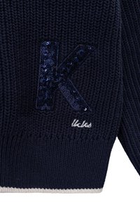 Marineblauer gestrickter Pullover mit einem großen, mit Pailletten bestickten "K" in Dunkelblau und dem gestickten "Kikks"-Logo in Weiß, mit einem kontrastierenden cremefarbenen Saum.