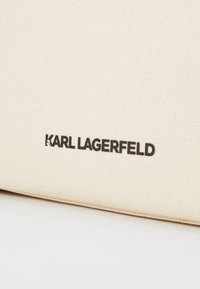 Beige canvasväska med svart "KARL LAGERFELD"-logotyp. Slät textur och en minimalistisk design utan ytterligare mönster.