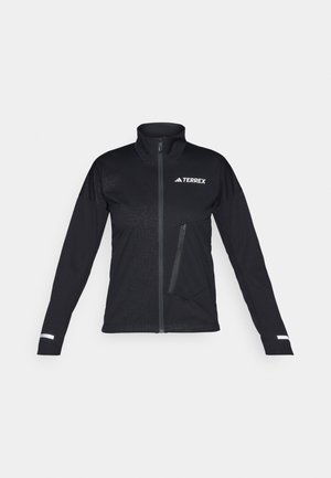 Veste softshell noire avec un col haut, fermeture éclair à l'avant, poche latérale, motif texturé sur le tissu et accents réfléchissants sur les manches.