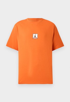 Oranžs kokvilnas T-krekls ar apaļu izgriezumu un īsām piedurknēm. Uz krūtīm ir melns Jordana logo baltā kvadrātā. Klasiskais piegriezums.