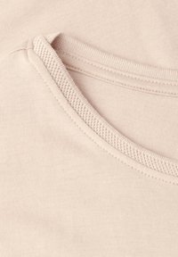 Gros plan d’une encolure en tissu beige avec une couture texturée détaillée autour du bord du col.