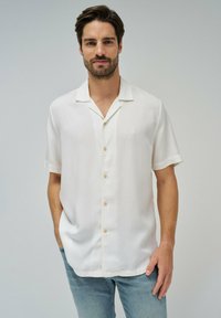 Camicia bianca a maniche corte con bottoni, realizzata in tessuto leggero e dalla vestibilità rilassata, caratterizzata da un delicato dettaglio di cuciture e colletto a scapitello.