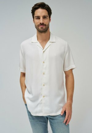 Camisa blanca de manga corta, de botonadura, confeccionada en una tela ligera con un corte relajado, que presenta un sutil detalle de costura y un cuello con muesca.