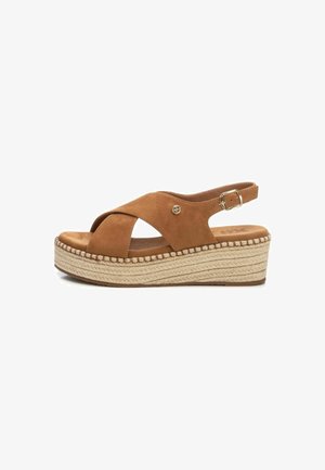 Sandalias de cuña de ante marrón con diseño de tiras cruzadas, correa de tobillo ajustable y suela de yute texturizada. Presenta un detalle del logotipo dorado.