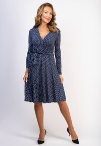 Marinblå om wrap-klänning med långa ärmar, med ett upprepande vitt geometriskt mönster. Slät tyg, utsvängd kjol och ett knytbart midjeband.