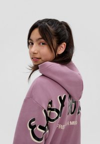 Hoodie violet avec un grand design de texte noir et crème au dos, doté d'une capuche et d'une texture douce. Coupe précise au niveau des épaules.