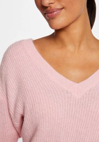 Pull rose doux en tricot avec un décolleté en V et un tissu texturé, doté d'une coupe décontractée et de poignets côtelés.