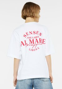 White oversized t-shirt made of cotton, featuring bold red text on the back: "SENSES THE LABEL AL MARE LIBERA" in a circular layout.