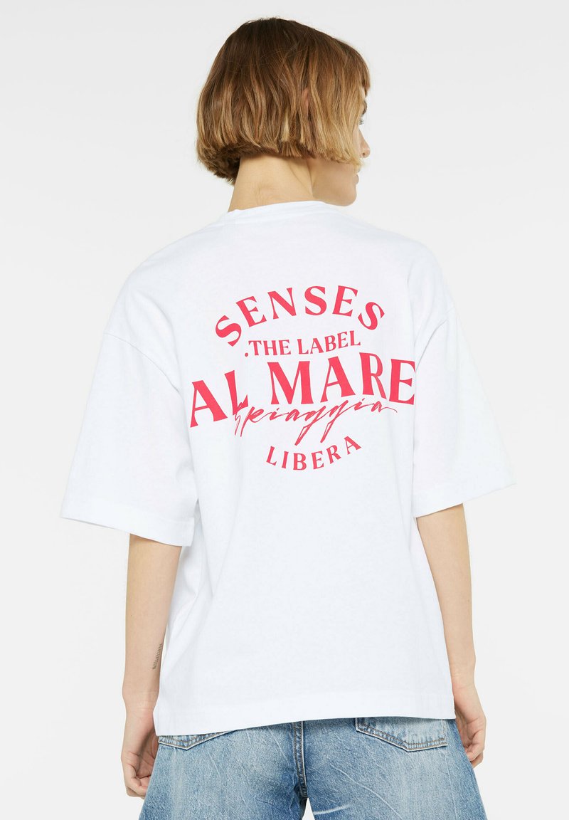 White oversized t-shirt made of cotton, featuring bold red text on the back: "SENSES THE LABEL AL MARE LIBERA" in a circular layout.