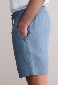 Pantaloncini azzurri realizzati in un tessuto morbido e strutturato, con vita elasticizzata e tasche laterali. Progettati con un taglio dritto e cuciture discrete.