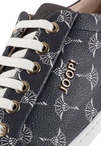 Sneakers navy en cuir texturé, avec un motif floral blanc, œillets dorés et lacets blancs, arborant un logo doré "JOOP!" sur le côté.