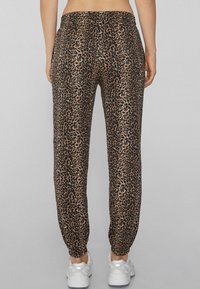 Leopardenmuster Jogginghosen mit einem elastischen Bund, schmal zulaufenden Knöcheln und einer glatten Textur. Kombiniert mit weißen Sneakern.