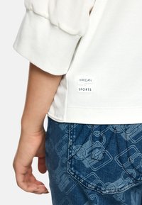 White sweatshirt with puffed sleeves, featuring a brand label. Pair of blue jeans with a subtle pattern and distinct pocket stitching details.