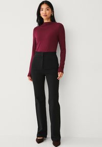 Bordeaux langemouwen top gecombineerd met hoge zwarte broeken. De outfit heeft een aansluitende silhouette en gladde texturen.
