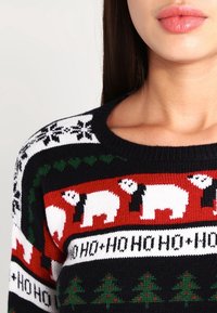 Pletený svetr s tmavě modrým základem, červenobílými vzory, ledními medvědy, sněhovými vločkami a malými zelenými stromečky. Kulatý výstřih a strukturovaná látka.