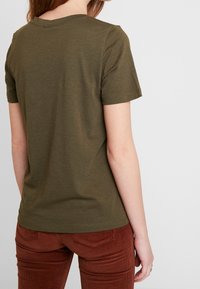 Olivově zelené tričko s krátkým rukávem a kulatým výstřihem, vyrobené z měkké látky, spárované s kalhotami z jemného kordu v barvě rezavé s vertikálními pruhy.