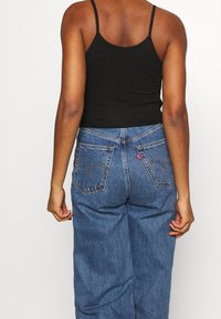 Top nero con spalline sottili abbinato a jeans in denim blu Levi's. I jeans presentano tasche posteriori classiche e dettagli di cucitura.