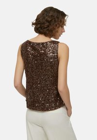 Top marrone con paillettes, design senza maniche, scollo rotondo e superficie strutturata. Indossato con pantaloni chiari dal taglio ampio e rilassato.