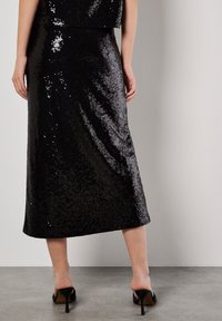 Zwarte pailletten midi-jurk met een rechte silhoutte. Beschikt over een zachte textuur en subtiele glans, gecombineerd met open teen hakken.