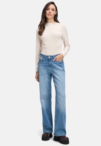 Helle beige Langarmbluse und hellblaue weit geschnittene Jeans. Die Jeans verfügen über ein klassisches Fünf-Taschen-Design und sind leicht ausgewaschen mit einer glatten Textur.