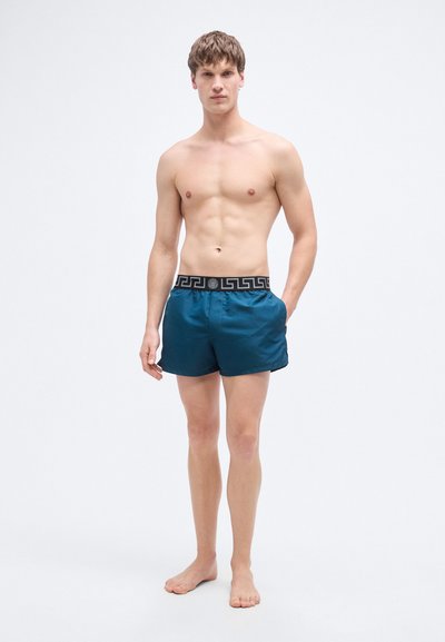 Ανδρικά μαγιό σορτσάκια σε τιρκουάζ ύφασμα με μαύρη ελαστική μέση που φέρει γεωμετρικό σχέδιο. Τα σορτσάκια έχουν μήκος μέχρι το μέσο του μηρού και είναι με λεπτή υφή.